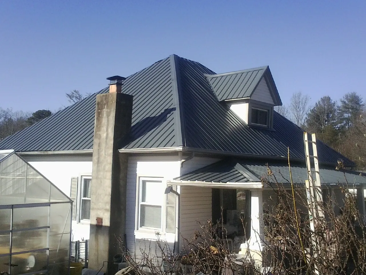 Dark blue standing seam metal roof on a white farmhouse with dormer — Slate & Tile Roof Repair by Roofing Brothers in Jonesville