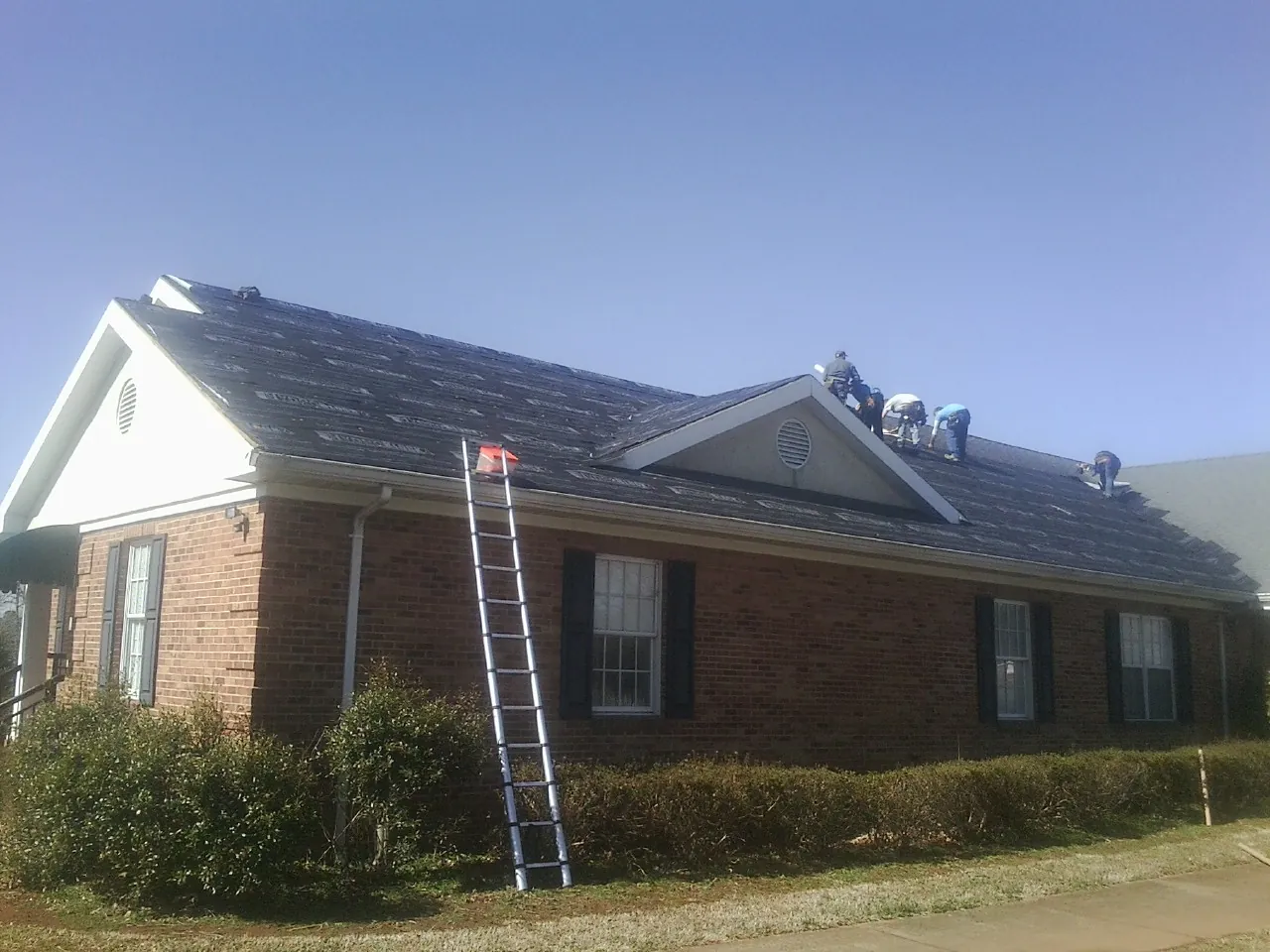 Crew tearing shingles off a brick ranch roof with a ladder set — Metal Roof Repair work by our crew in Jonesville