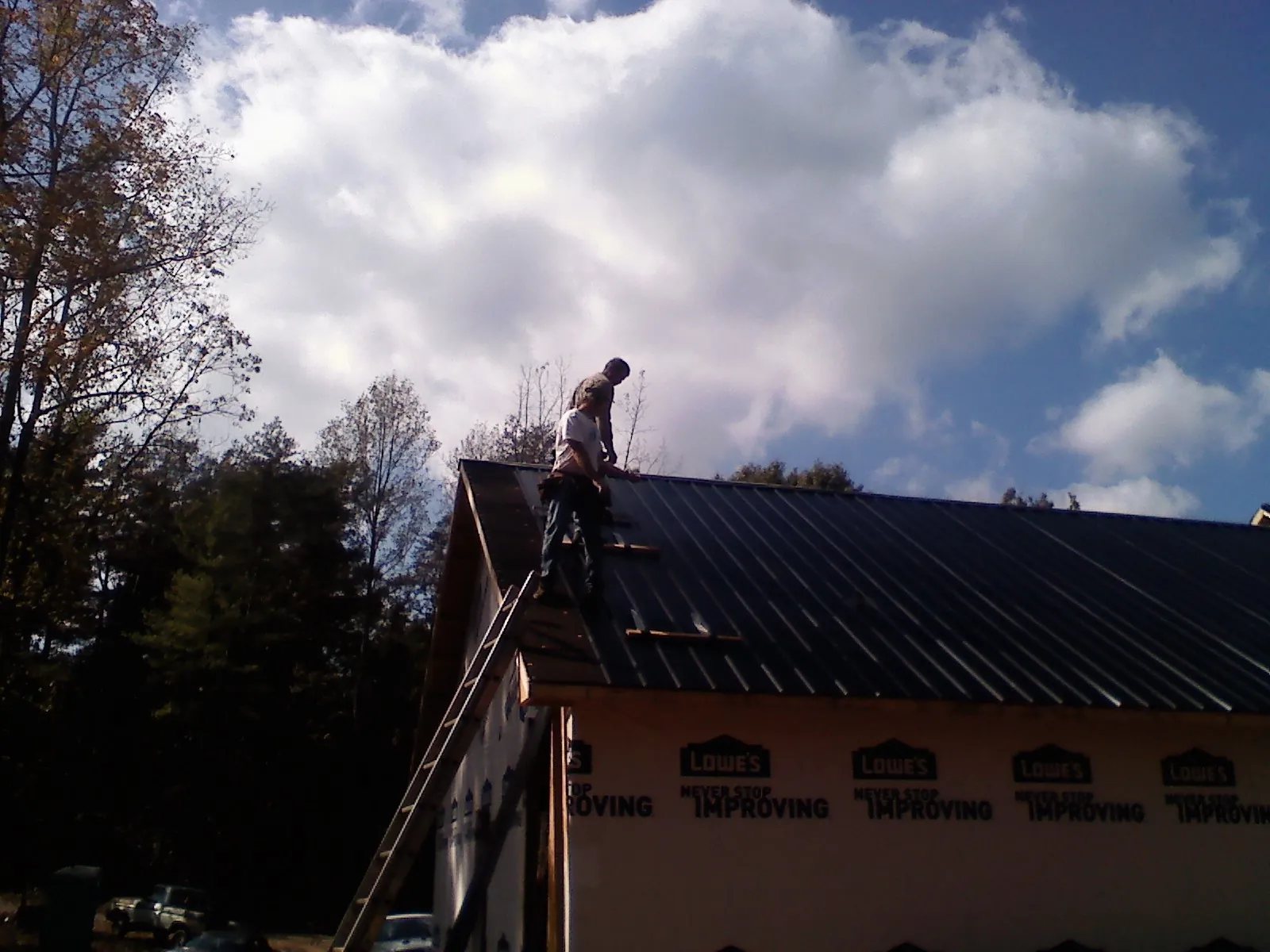 Roofer fastening dark metal panels high against a cloudy sky, from a Roof Inspection job in Jonesville